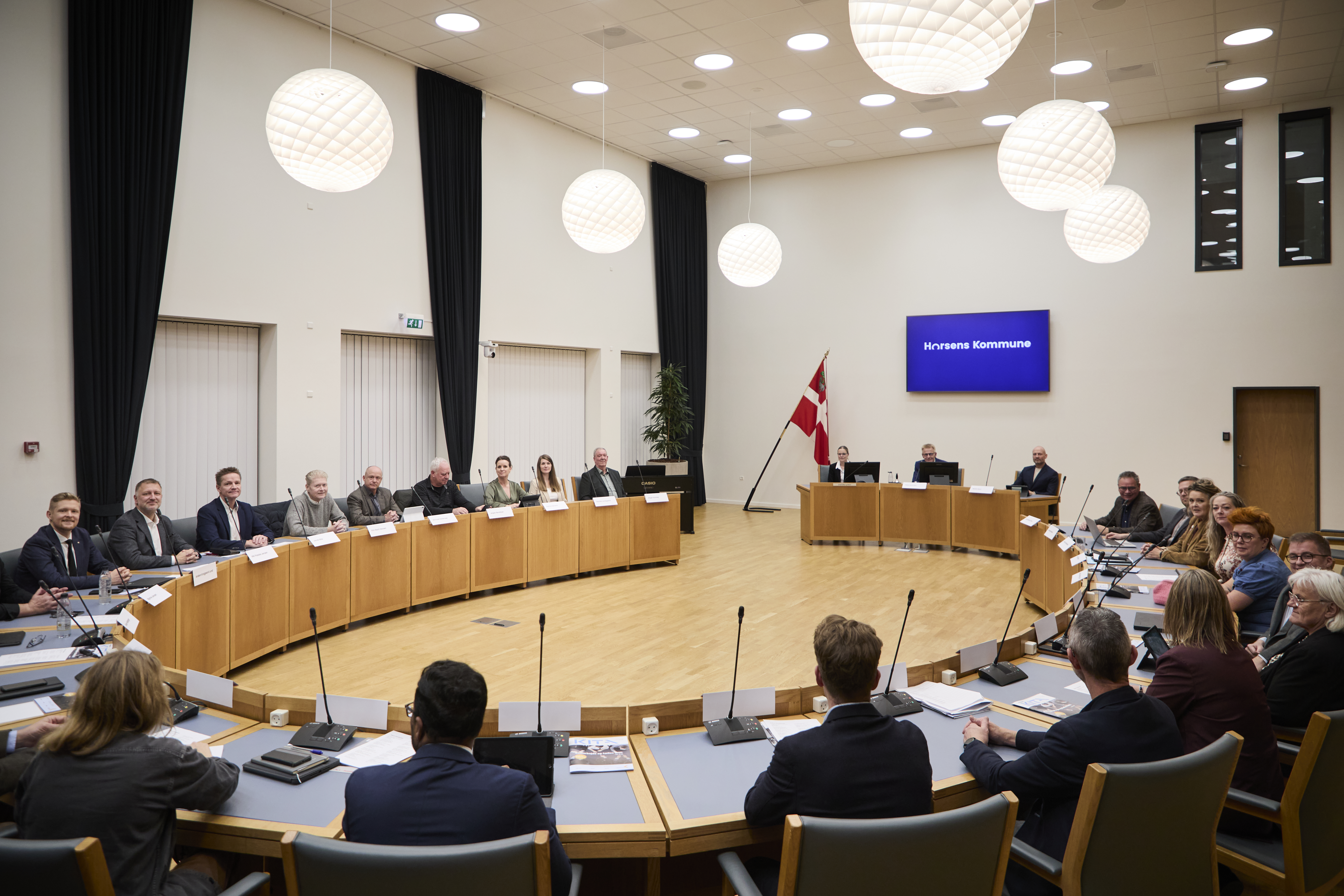 Billede af byrådssalen med byrådspolitikere siddende til møde. 
